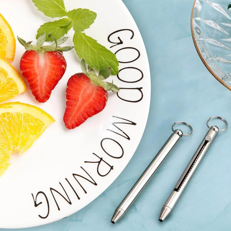 A titanium keychain toothpick set rests on a white plate surrounded by fresh strawberries and orange slices.
