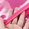 A hand holds a bright pink wig storage bag with a hanger against a pink background.