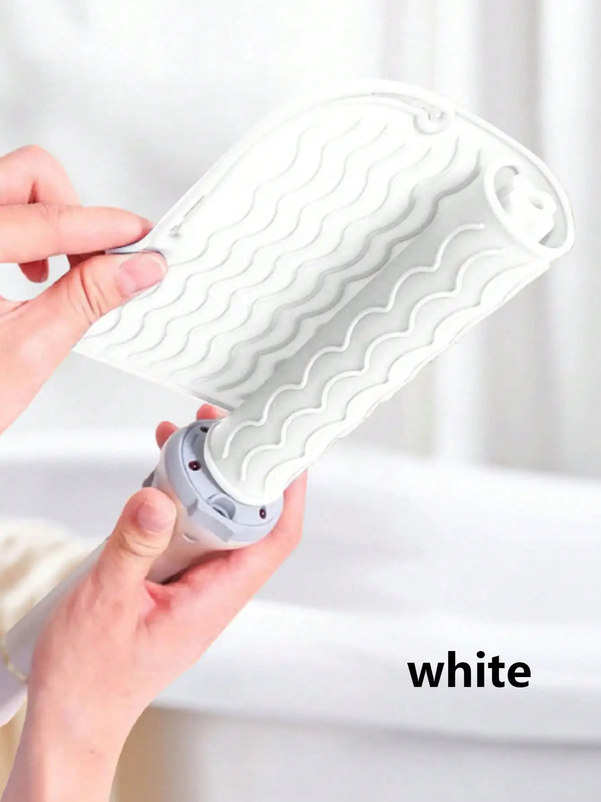 A hand is holding a white silicone heat resistant mat for hair styling tools, showing its textured surface.