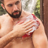 Un homme utilise une éponge exfoliante colorée et réutilisable pour le corps sur sa peau avec de l'eau.