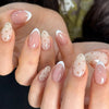 Close-up of hands displaying light pink and white almond shaped press-on nails with scattered gold dots.