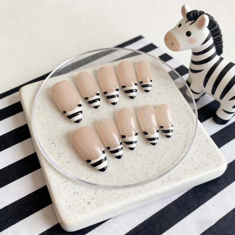 Un set de uñas postizas con rayas de cebra, exhibidas sobre un cristal transparente con fondo a rayas blancas y negras.
