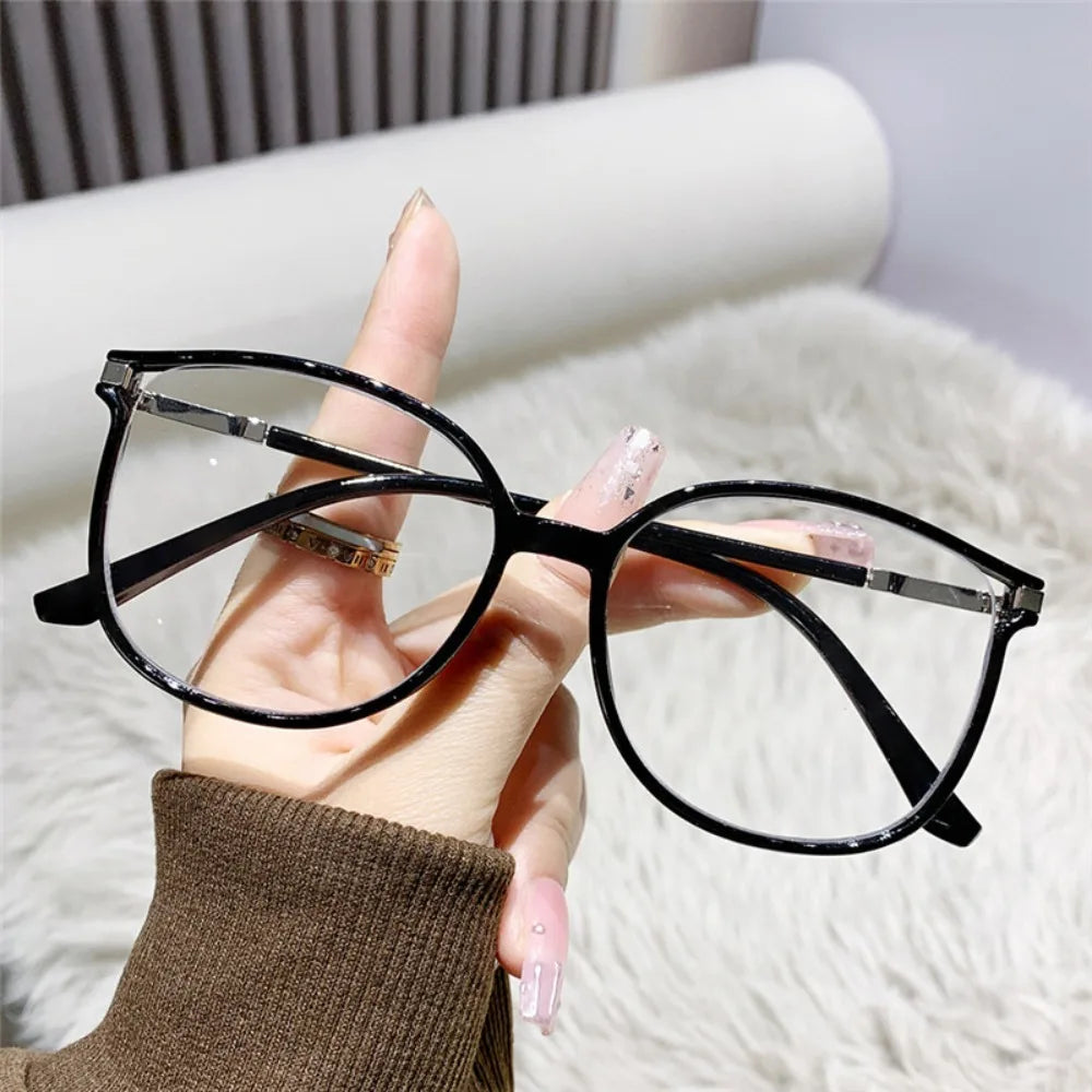 Lunettes de lecture à monture noire posées sur les doigts d'une personne sur un fond blanc et duveteux.