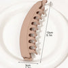 A beige banana hair clip is shown on a white plate, illustrating its size and shape.