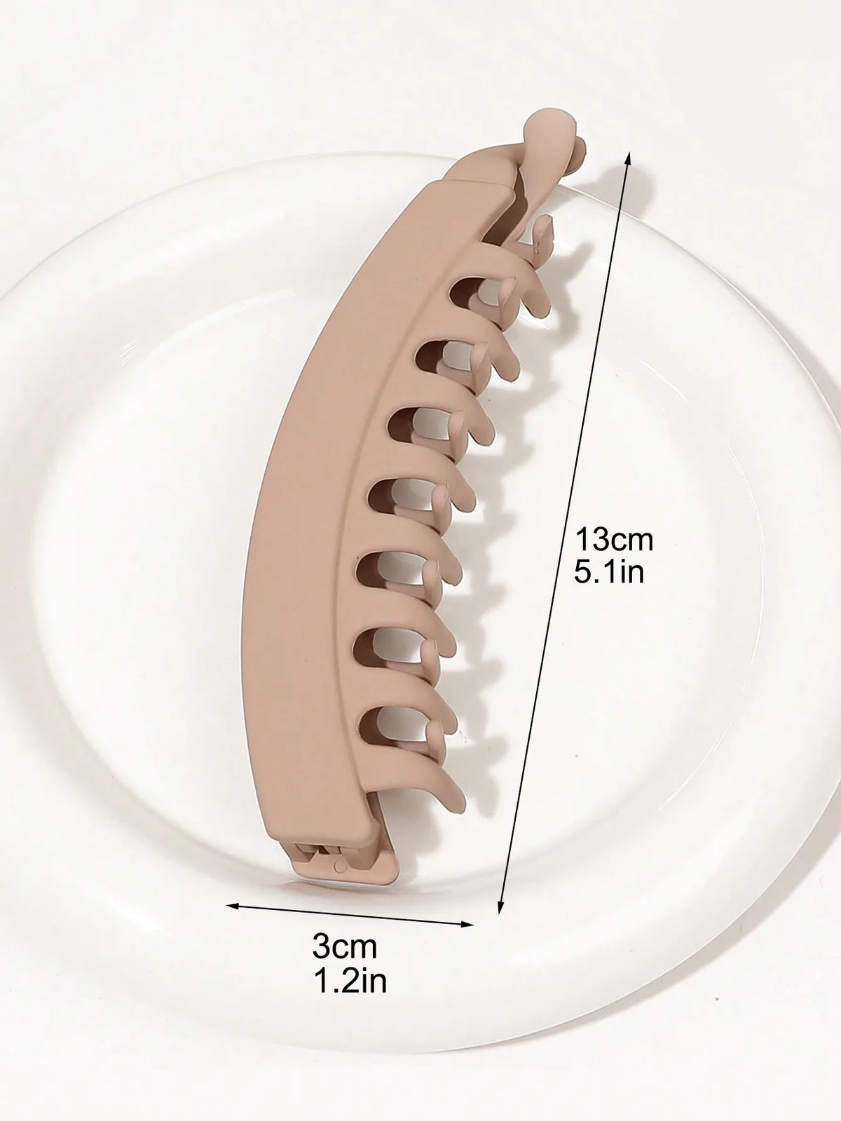 A beige banana hair clip is shown on a white plate, illustrating its size and shape.