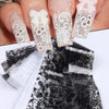 Une main montre des autocollants de faux ongles en dentelle blanche et noire sur les ongles, avec un tissu en dentelle noire 