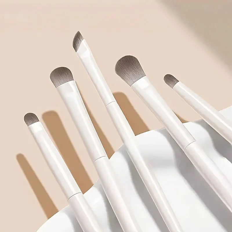 A set of five professional makeup brushes with light gray and white handles displayed on a white surface.