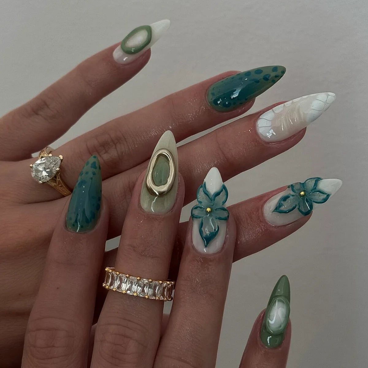 A hand displaying a set of 24 press-on almond nails featuring various designs including floral and butterfly motifs in shades