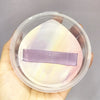A translucent storage box containing a lavender makeup puff or sponge.