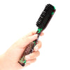 A hand holds a black and green professional beard styling brush with dark bristles.