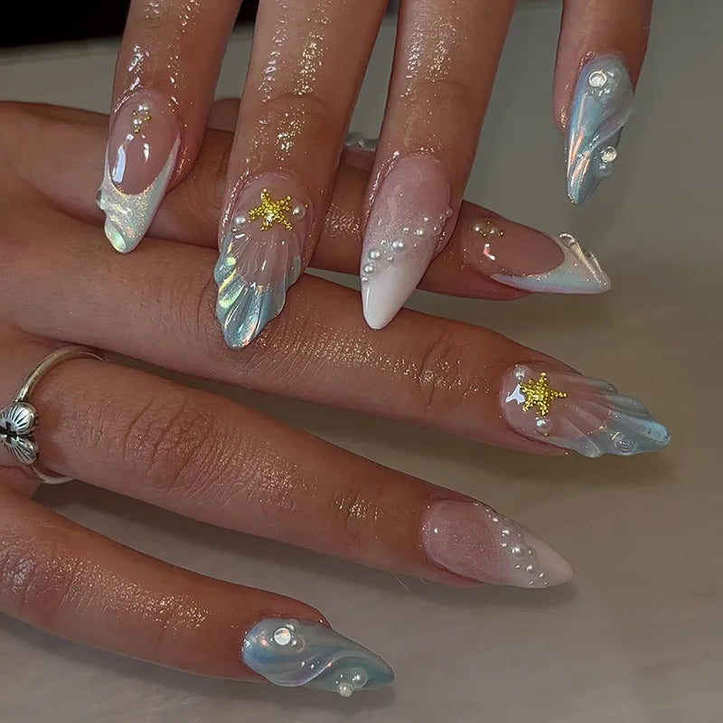 A close-up of a hand displaying 24-piece almond press-on nails with iridescent blue and white floral and butterfly designs.