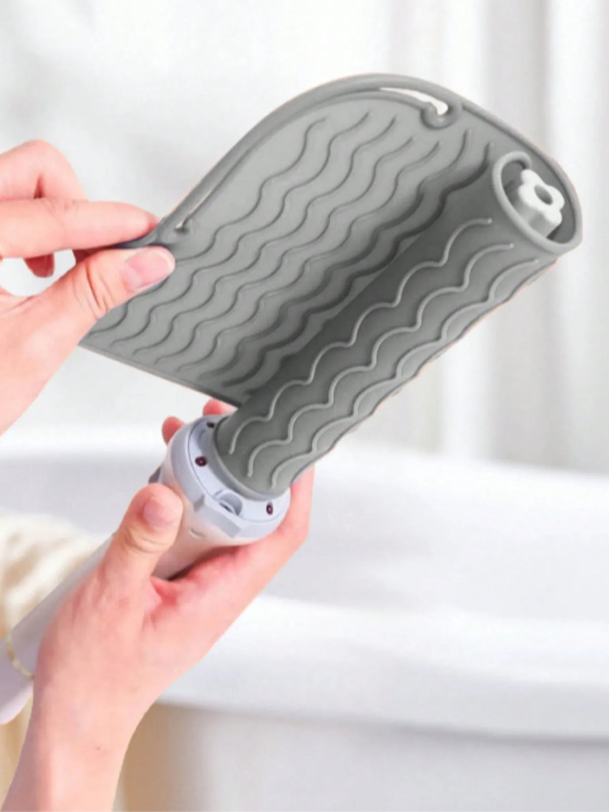 A hand holds a gray silicone heat resistant mat for hair styling tools, showing its textured surface.