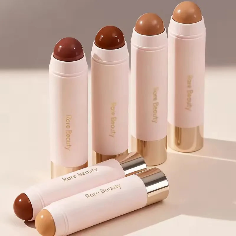A set of Rare Beauty liquid bronzer contour foundation sticks in various shades and packaging.