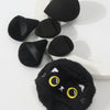 Un ensemble de poudres noires en forme d'oreilles de chat, présentées sur une surface blanche.