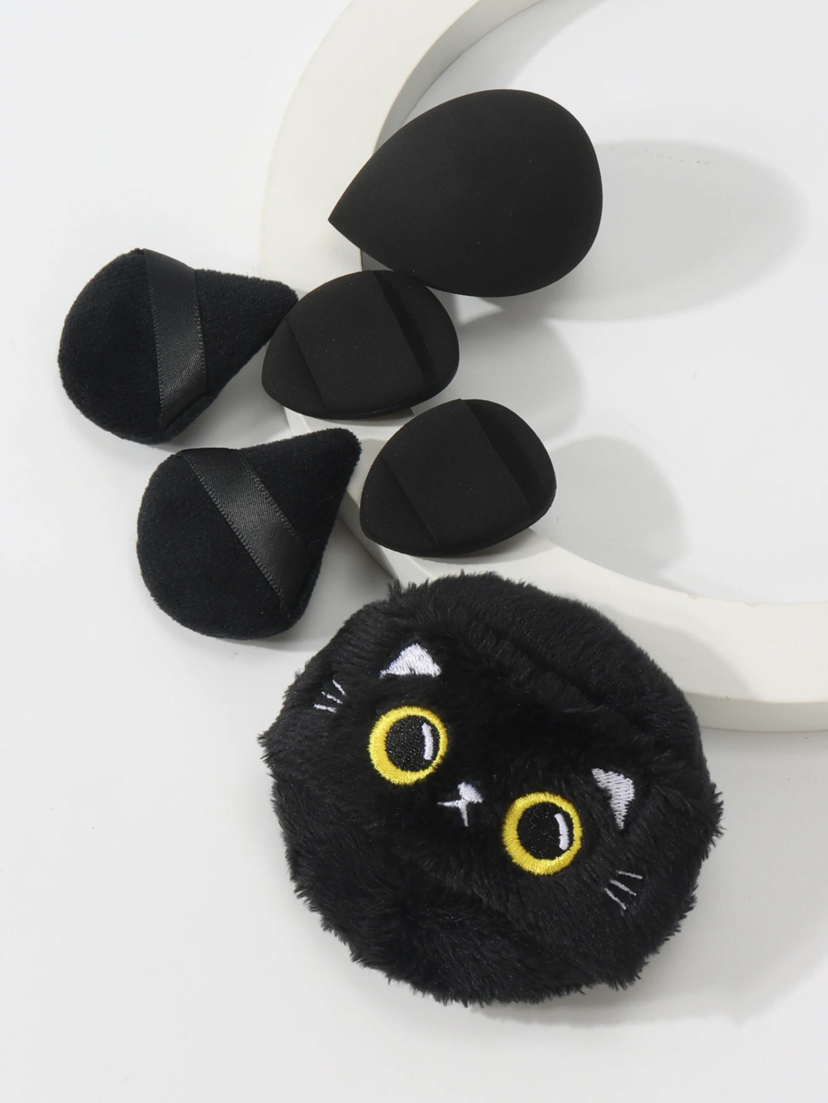 Un ensemble de poudres noires en forme d'oreilles de chat, présentées sur une surface blanche.