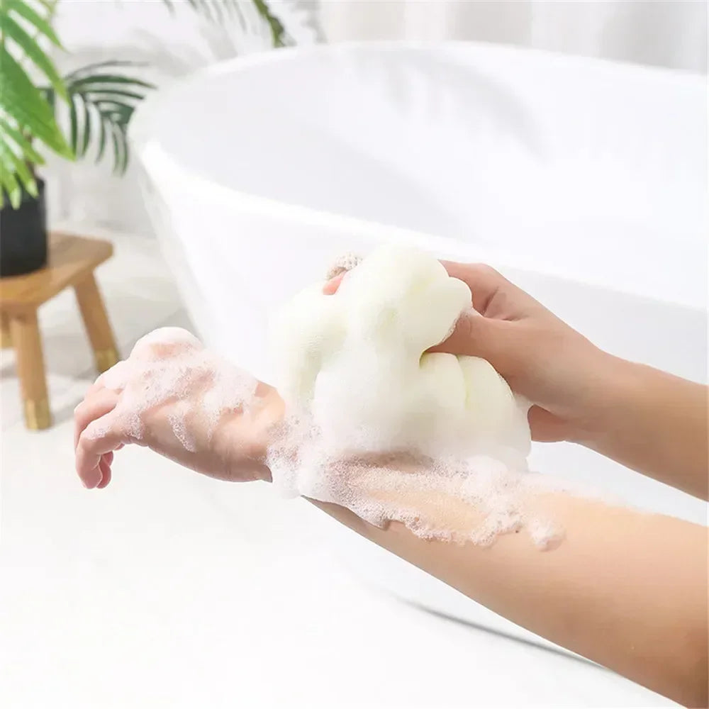 A hand is squeezing a large white exfoliating bath bubble ball onto the palm of another hand.