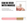 A pink eyelash extension cleaning brush with a white handle and gold accents shown next to a hand.