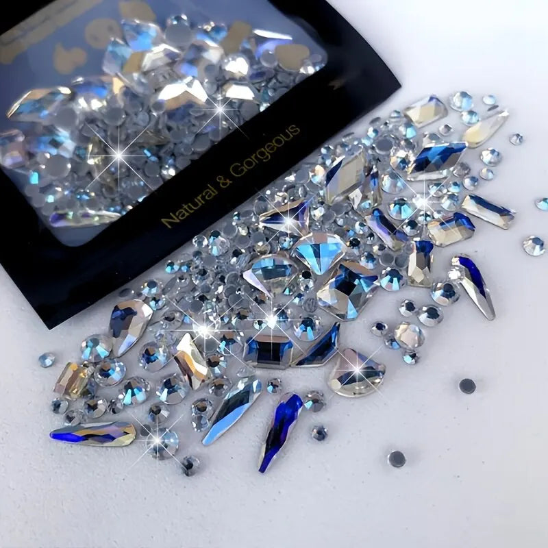 A pile of mixed glass rhinestones in various shades of blue and clear, displayed next to the product packaging.