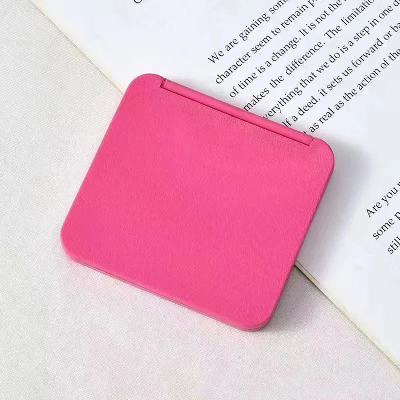 A bright pink double-sided portable makeup mirror resting on a white page with text.