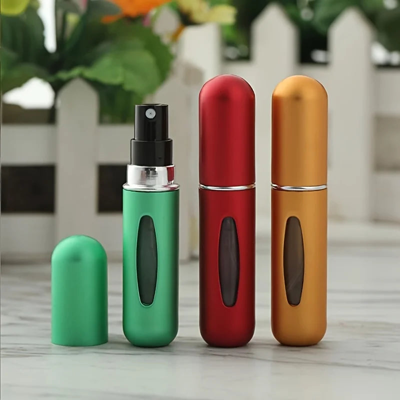Three mini refillable perfume atomizer bottles in green, red, and gold standing on a white surface.