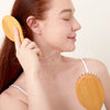 A woman is using a wooden hair brush on her hair, demonstrating its use for detangling or scalp massage.
