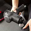 A hand is holding a black deep tissue massage gun with a textured head, positioned for use.