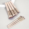 A set of seven professional makeup brushes with light pink handles and fluffy synthetic bristles arranged on a white surface.
