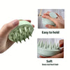 A hand is holding a light green silicone body and scalp massage brush, demonstrating its easy to hold and soft features.