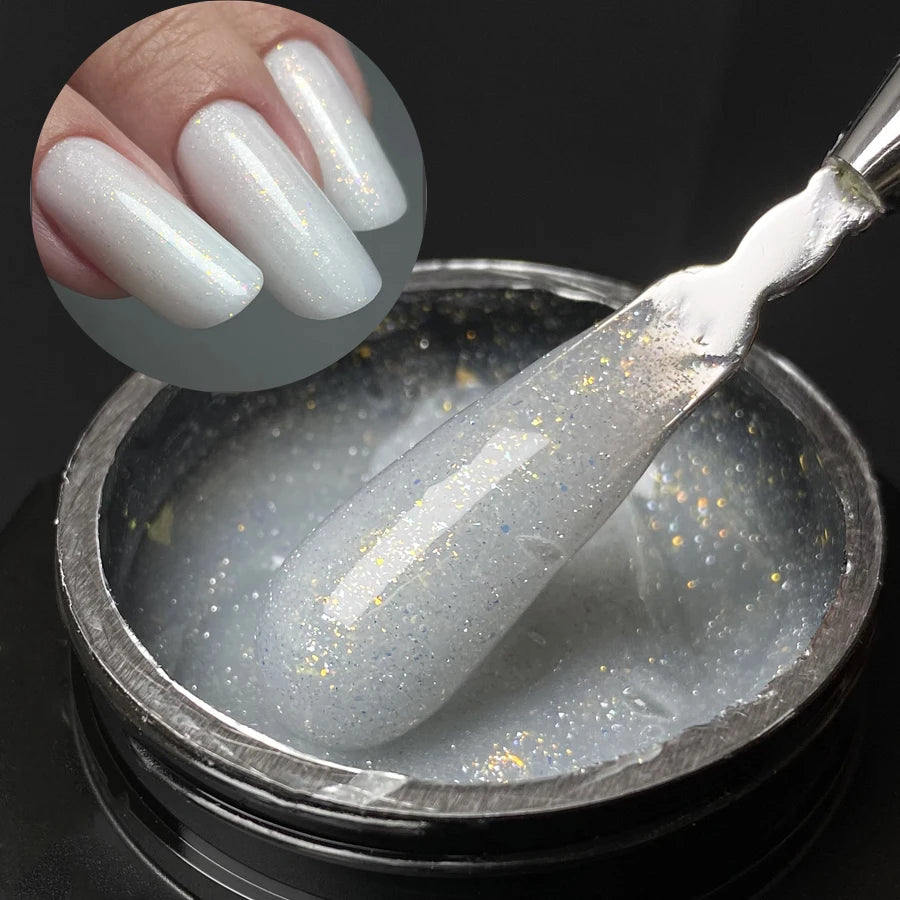 Un outil argenté plonge dans un pot de gel de construction blanc et pailleté pour extensions de ongles.
