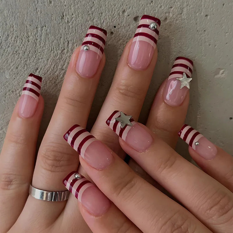 A hand displaying gothic Y2K press-on nails with red and white stripes and silver star accents.