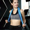 A woman wearing a black sports top and bottoms holds a blue towel in a gym setting.