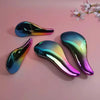 A set of three iridescent silicone detangling hair brushes displayed on a pink background.