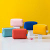 A collection of colorful waterproof PU leather makeup bags in pink, blue, orange, and yellow displayed on a white surface aga