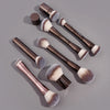 A set of four double-ended makeup brushes with silver and black handles and fluffy synthetic bristles on a gray background.