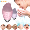 A pink and gray USB rechargeable facial cleansing brush being used on a woman's face.