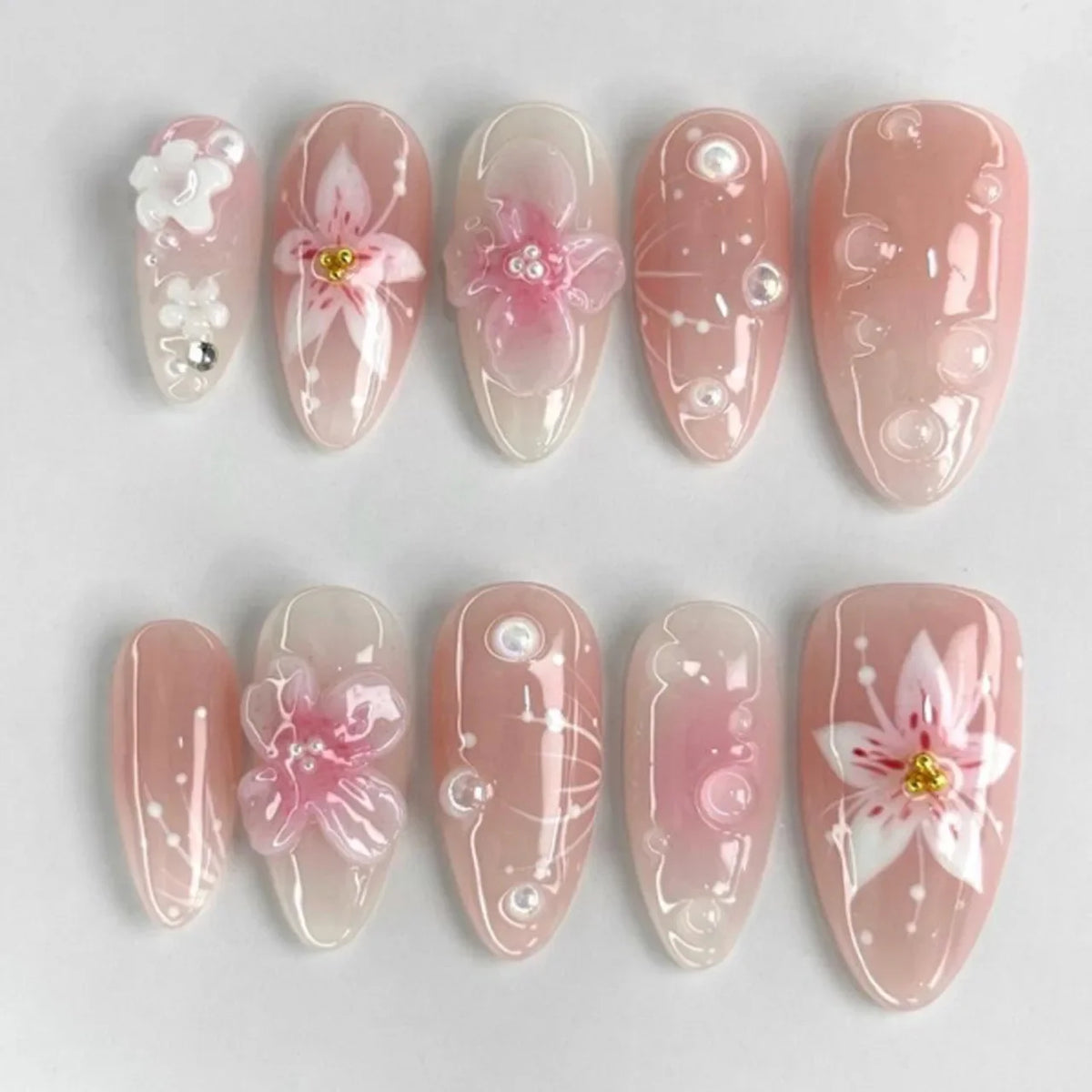 Un set de 24 ongles press-on en amande avec des motifs floraux roses et blancs et des accents de perles.