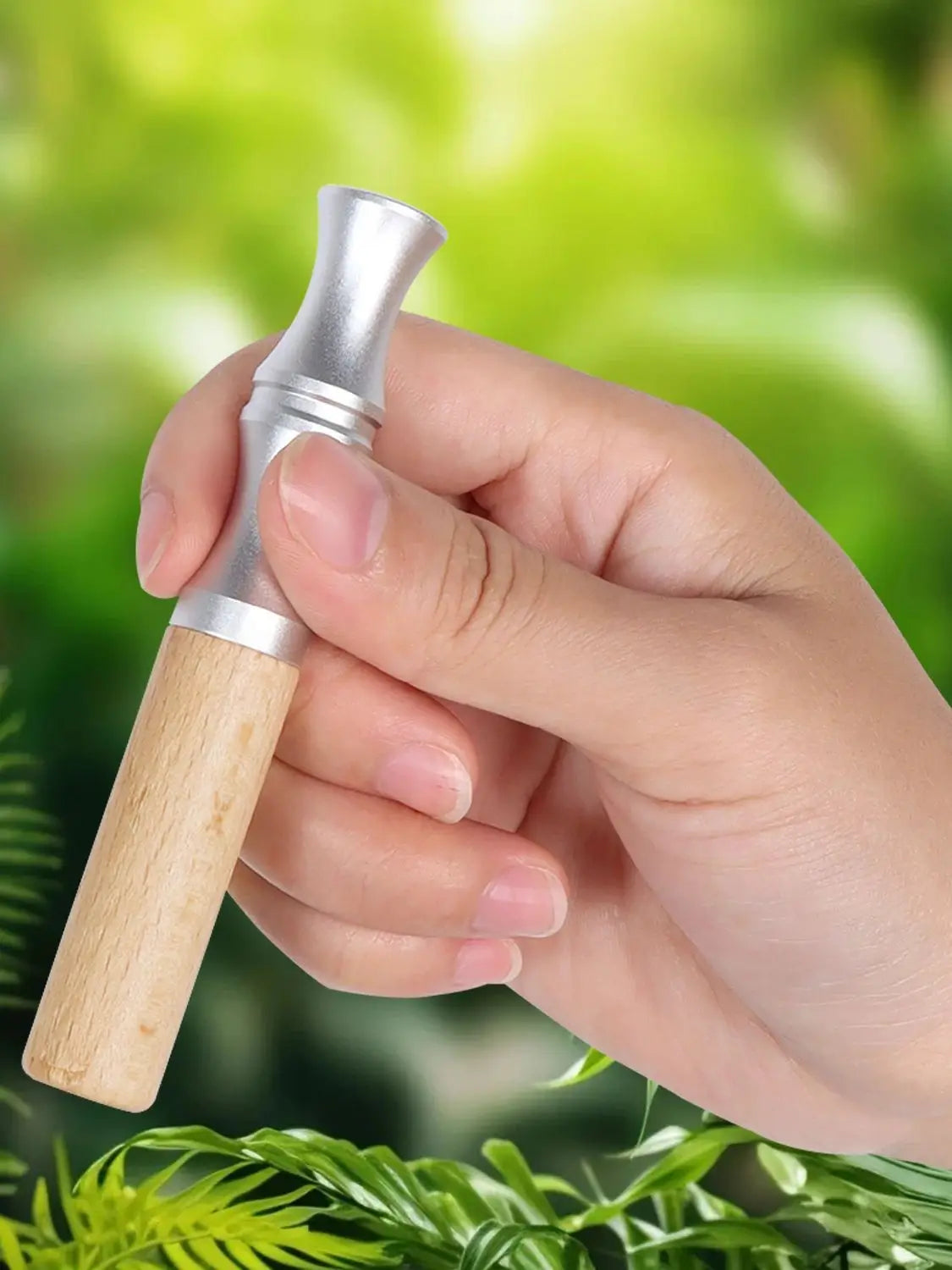 A hand holds a natural wooden stop smoking stick diffuser with a silver cap against a blurred green background.