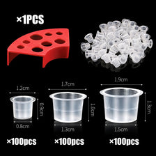 A set of tattoo ink cups including a red holder and three sizes of clear disposable cups.
