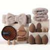 A set of makeup brushes and tools displayed on a white surface with fluffy gray fabric and brown sponges.