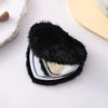 A heart-shaped foldable travel makeup mirror covered in black faux fur resting on a white surface.