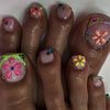 A close-up photo of several fingers displaying press-on fake nails with floral designs and glitter accents.
