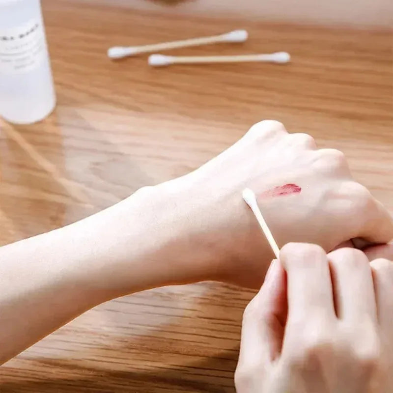 Eine Hand verwendet einen doppelseitigen Holz-Wattestäbchen, um roten Pigment auf die Haut aufzutragen.