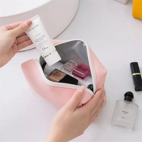 A hand holds a Dior powder compact and a pink PU leather makeup bag containing various cosmetic items.
