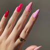 A hand displaying 24 press-on false nails with a French wavy design in shades of pink and magenta.