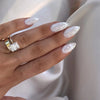A hand displaying elegant white almond shaped press-on nails with subtle glitter accents.