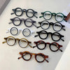 Collection de lunettes de lecture claires réglables, différentes montures et couleurs, disposées sur une surface blanche.