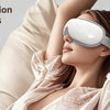 A woman is using a white eye massager device while relaxing on a couch.