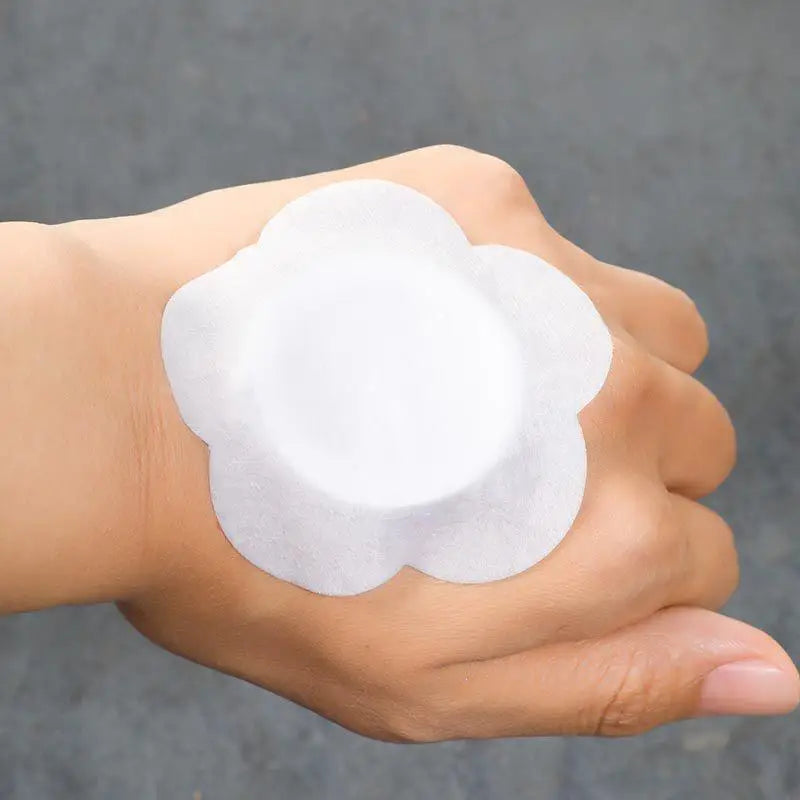 A hand is holding a white, disc-shaped adhesive belly button patch.