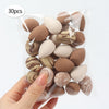 A hand holds a clear plastic bag containing 30 reusable expandable makeup sponges in various natural and earth tones.