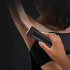 A hand holds a black electric hair trimmer against a person's arm for hair trimming.